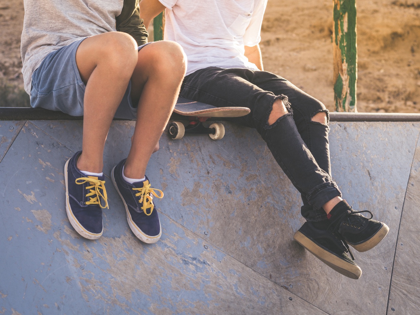 Zwei Jugendliche sitzen mit Skateboard auf einer Rampe