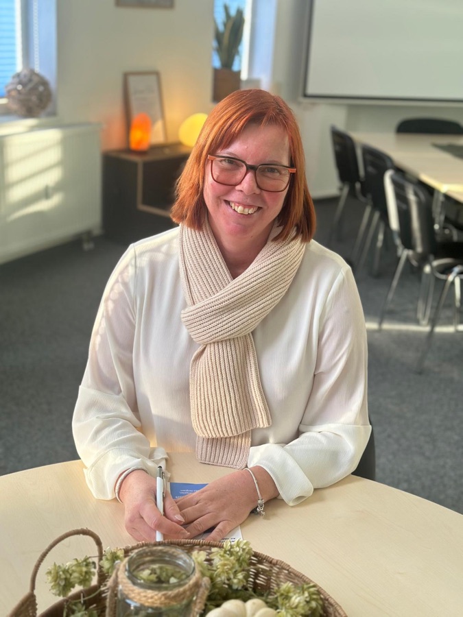 Melanie Kolbe sitzt lächelnd an einem Tisch im Büro